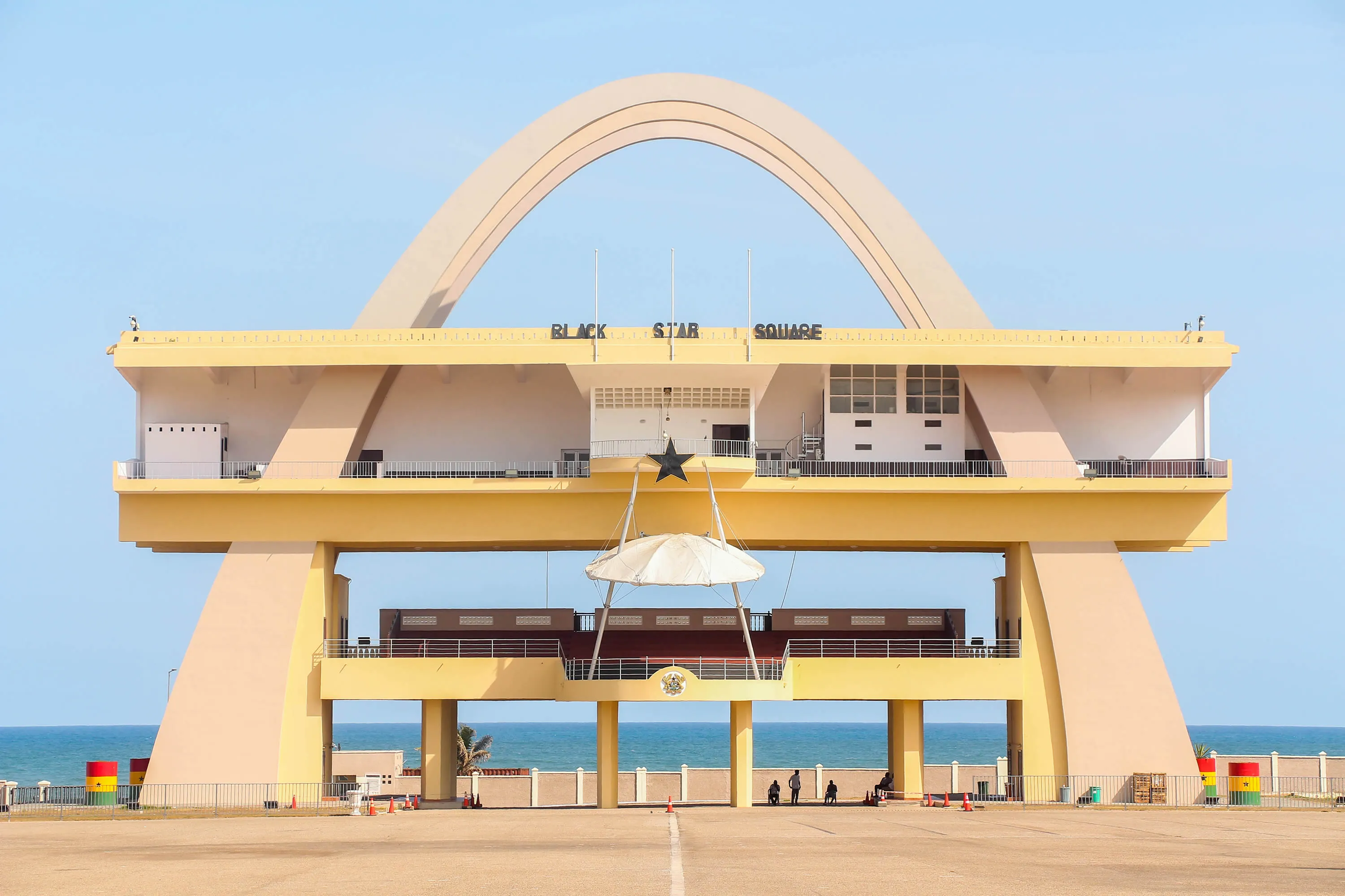 An elegant modernist arch reaches over Black Star Square in Ghana with the sea behind it.