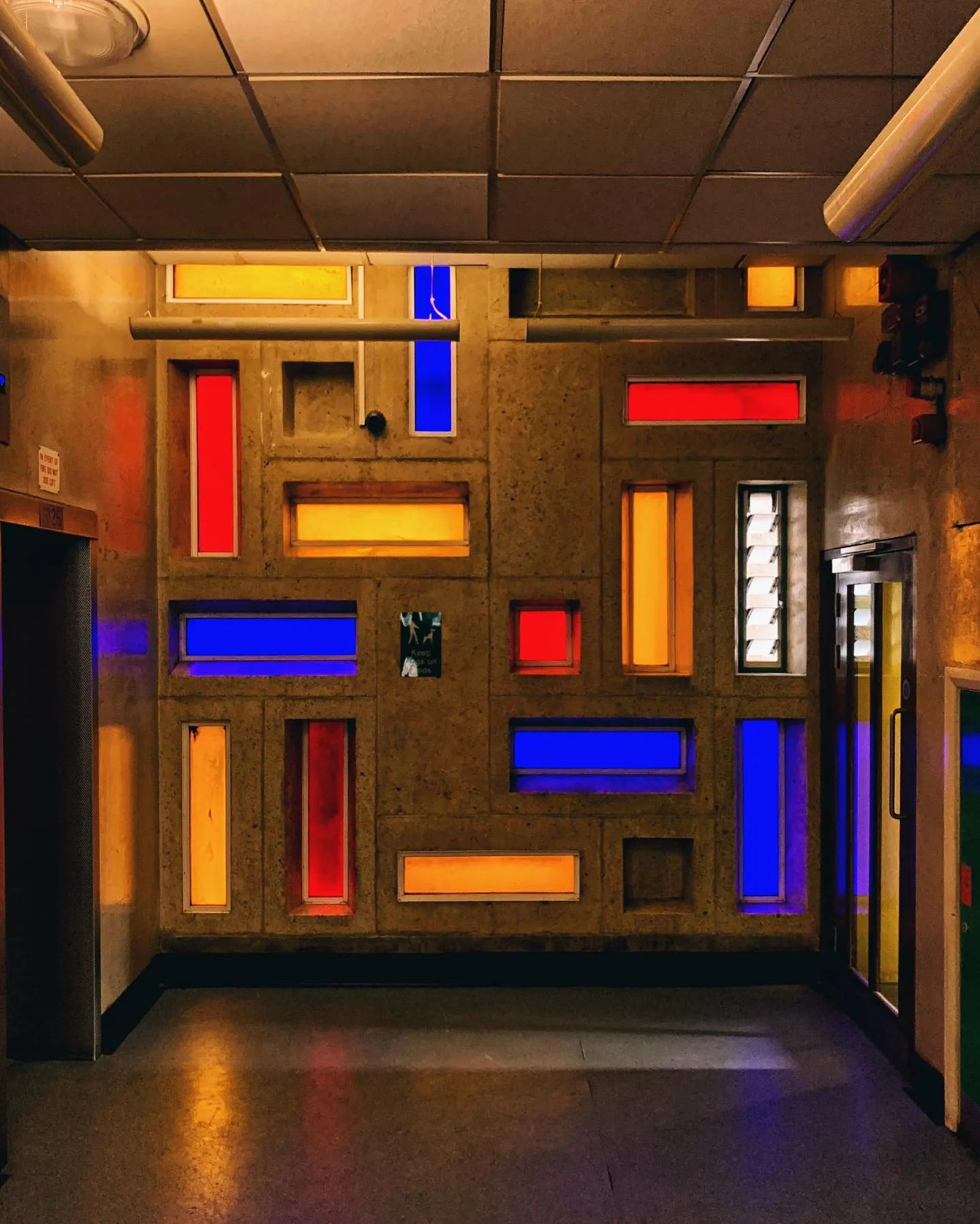 A warm concrete wall punctuated with lowing red, blue and orange windows..