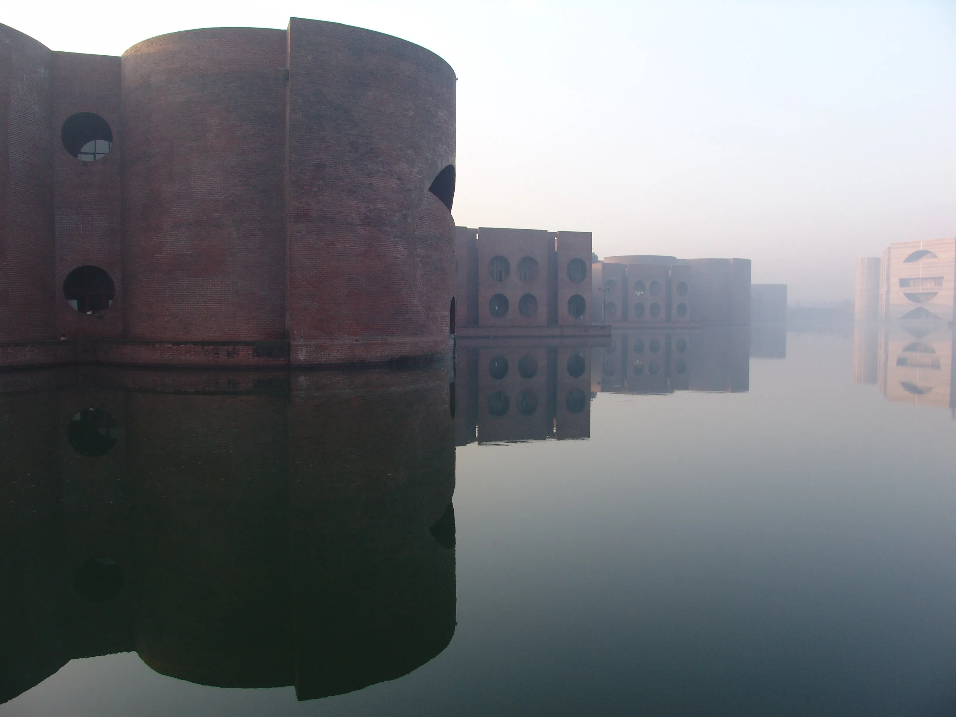 Louis Kahn's National Assembly of Bangladesh in Dhaka, its brick and concrete masses pierced by vast circular openings and mirrored in the surrounding lake