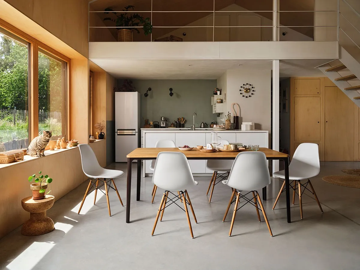 An open plan dining room furnished with six Eames DSW chairs around a wooden dining table.