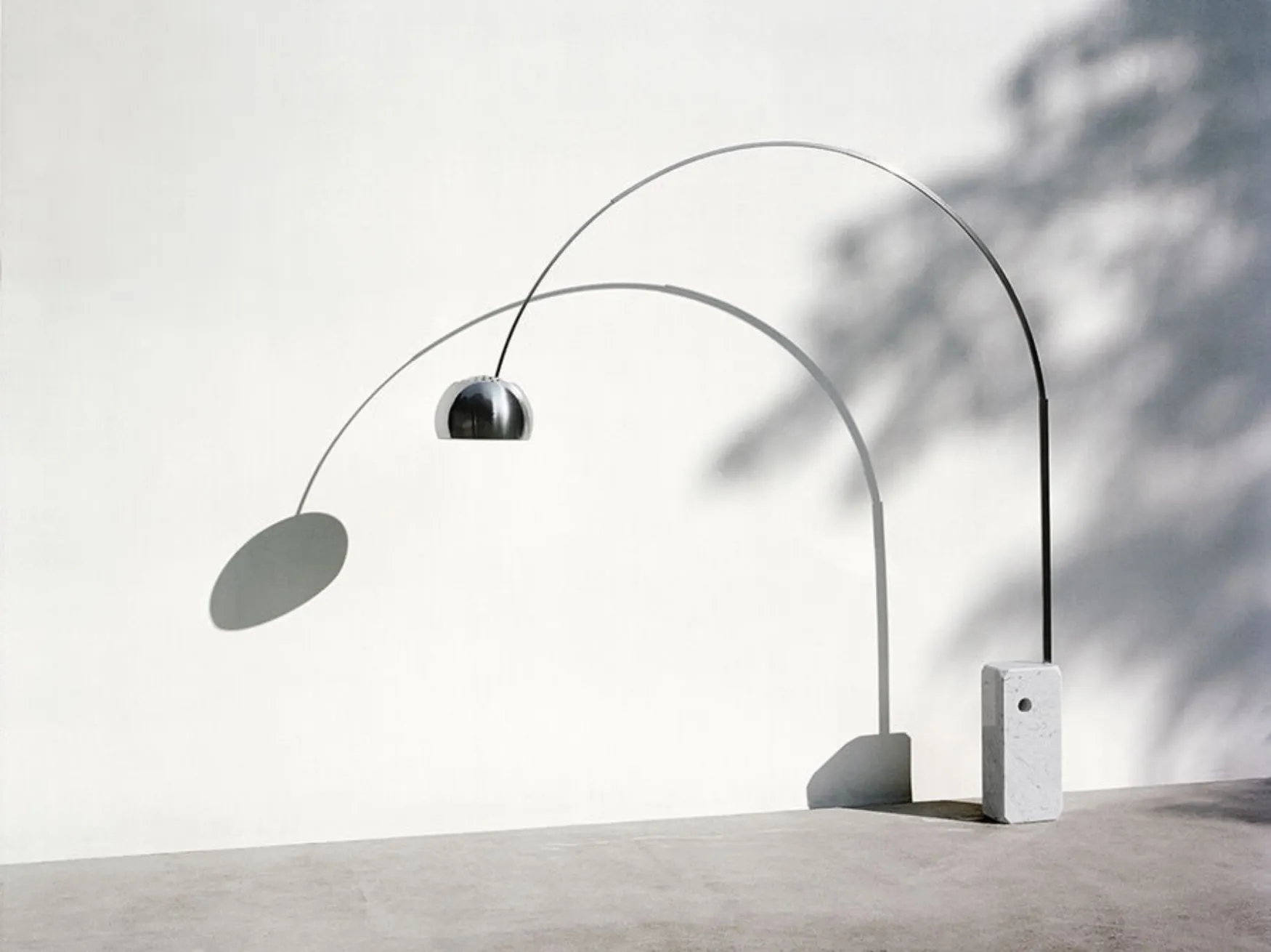 The sweeping steel arc of an Arco-style floor lamp rising from a pale marble base, lit in warm tones.