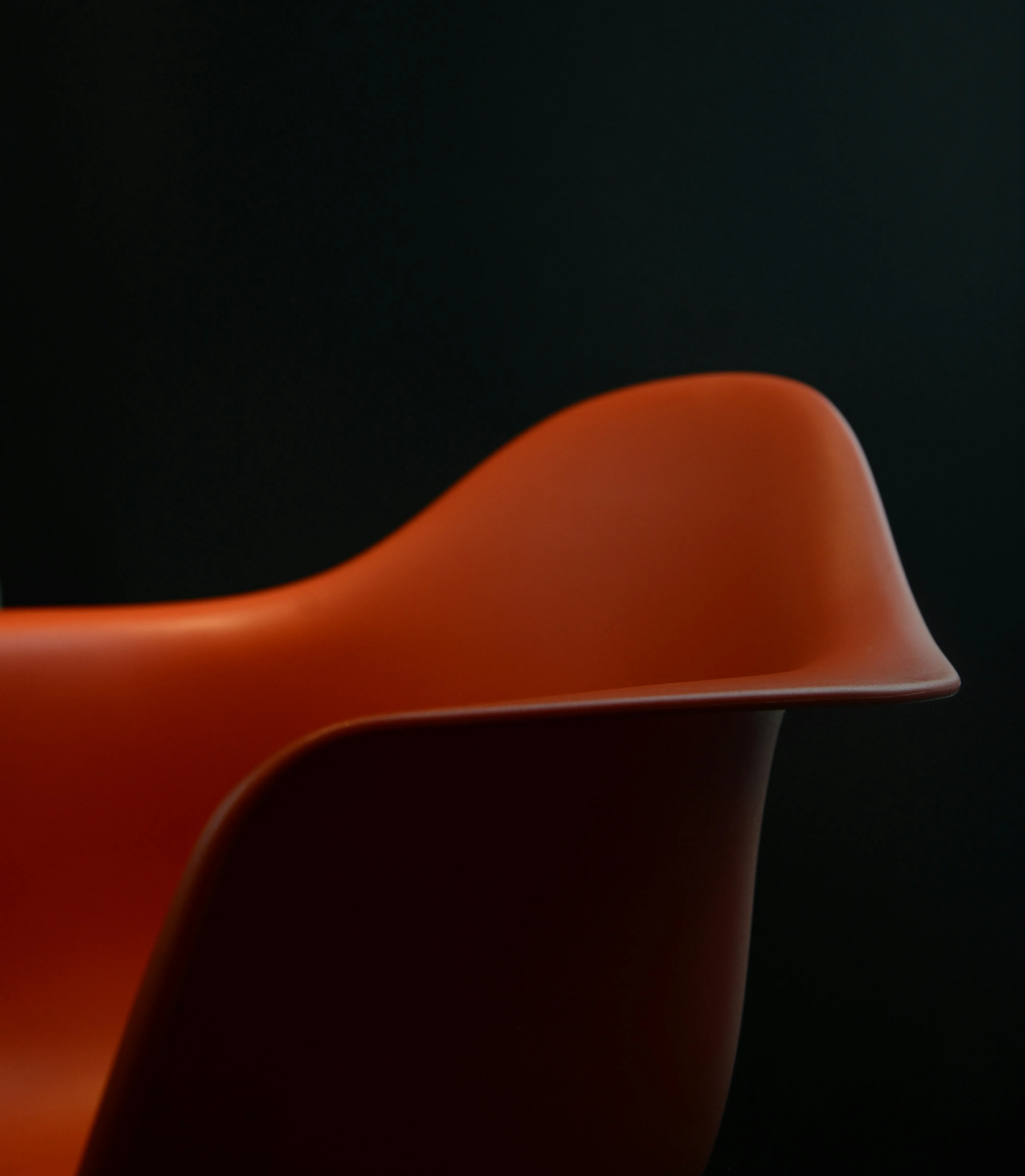 A moody shot of the sinuous lip of an Eames chair, taken against a dark background.