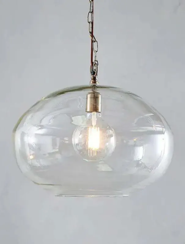 Nkuku Otoro clear recycled-glass pendant lit above a timber island, visible bubbles in the glass