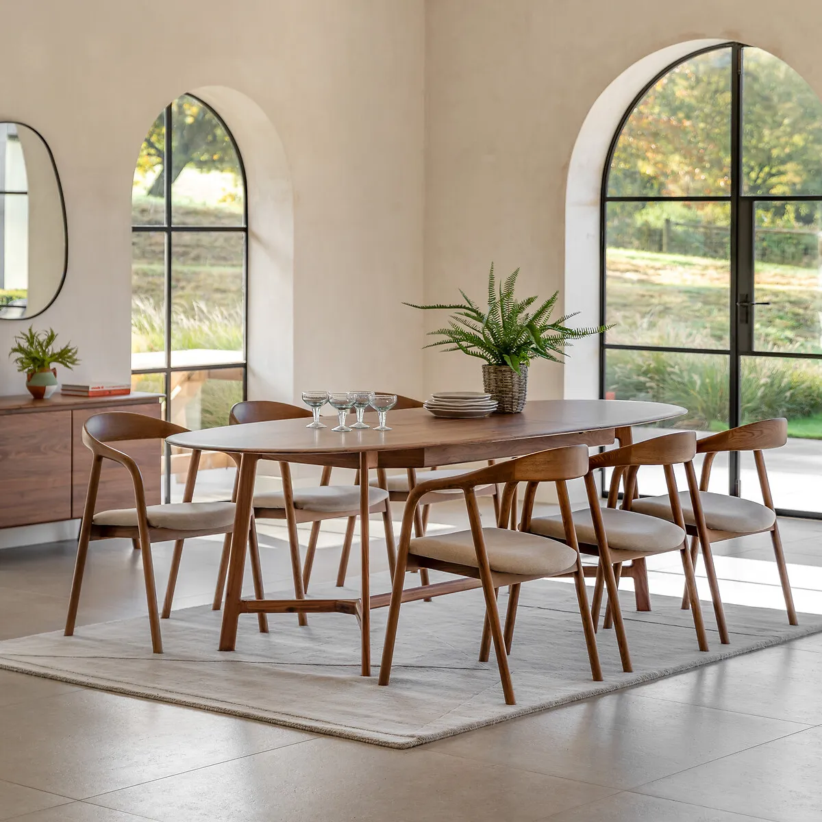 A walnut dining table, in a room flooded with sunlight and with matching walnut chairs.