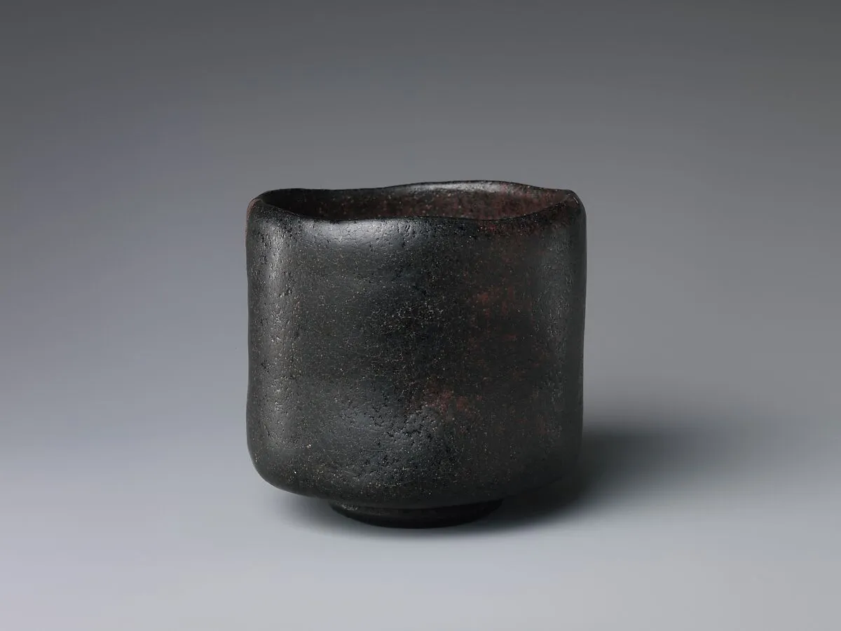 A small black lightweight glazed earthenware tea bowl, molded by hand rather than thrown on a potter's wheel.